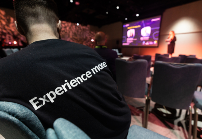 A man sitting in a conference room with a t-shirt that says experience more, showcasing his expertise in Event Design.